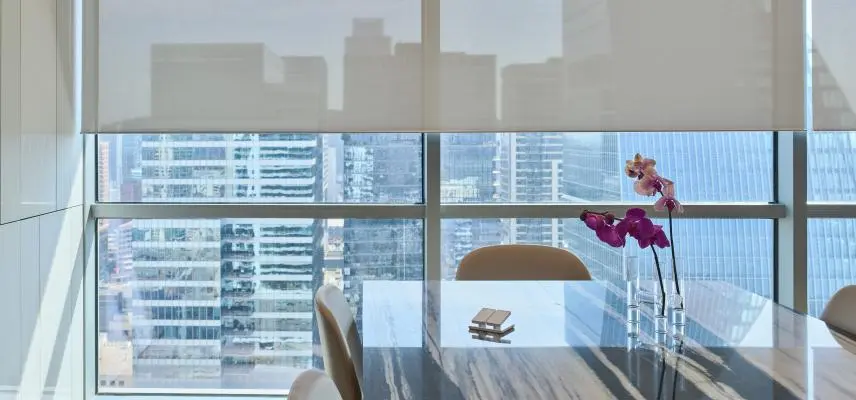 Motorized Lutron roller shades over floor-to-ceiling windows with a city view